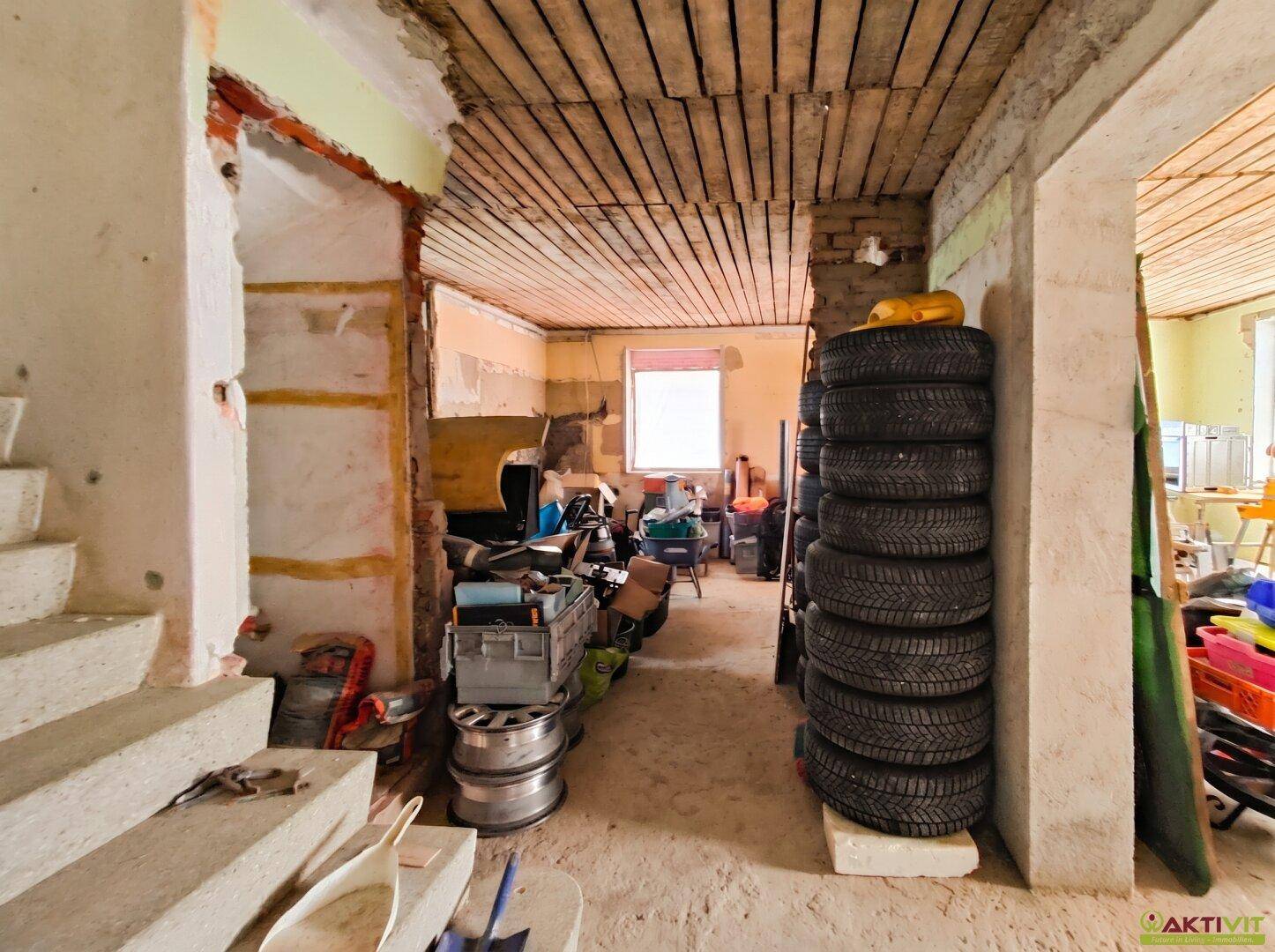 Unfertiger Kellerraum mit gestapelten Reifen, Baumaterialien und sichtbarer Holzdecke.