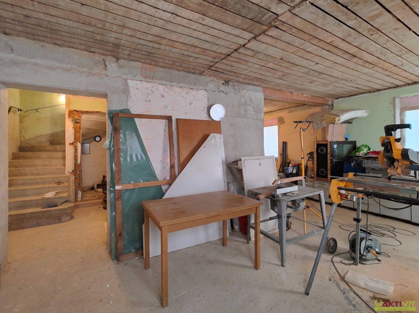Unfertiger Kellerraum mit Werkzeugen, Baumaterialien und sichtbarer Holzdecke.