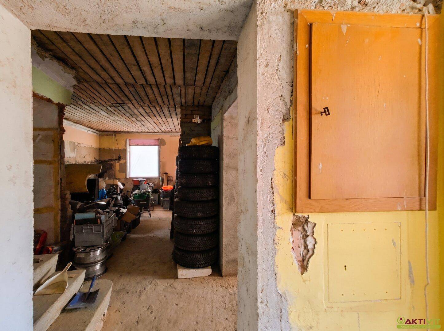 Blick in einen unfertigen Kellerraum mit gestapelten Reifen und einer Holztür.
