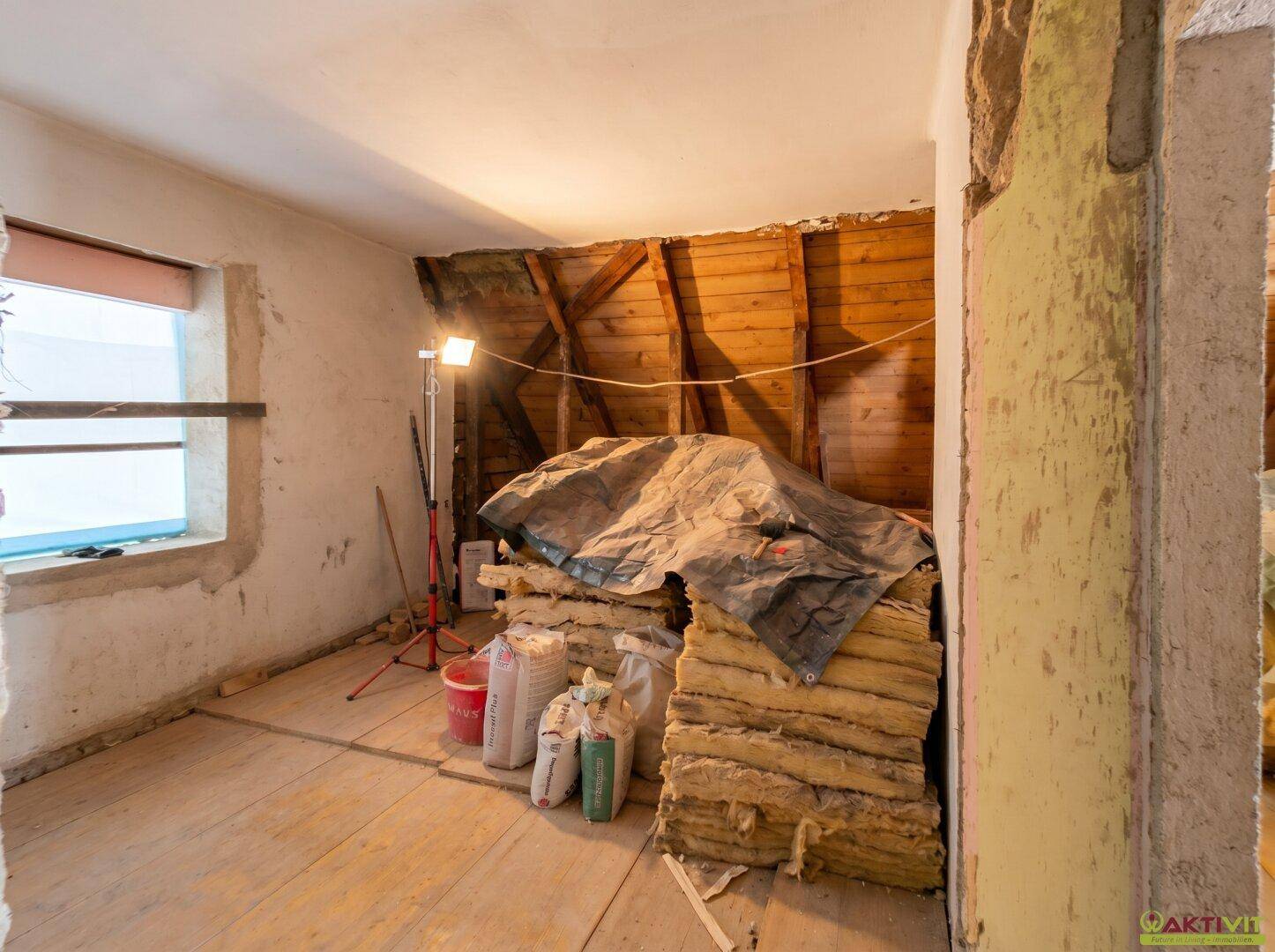Unfertiger Innenraum mit sichtbaren Holzbalken und Baumaterialien, bereit für den Ausbau.