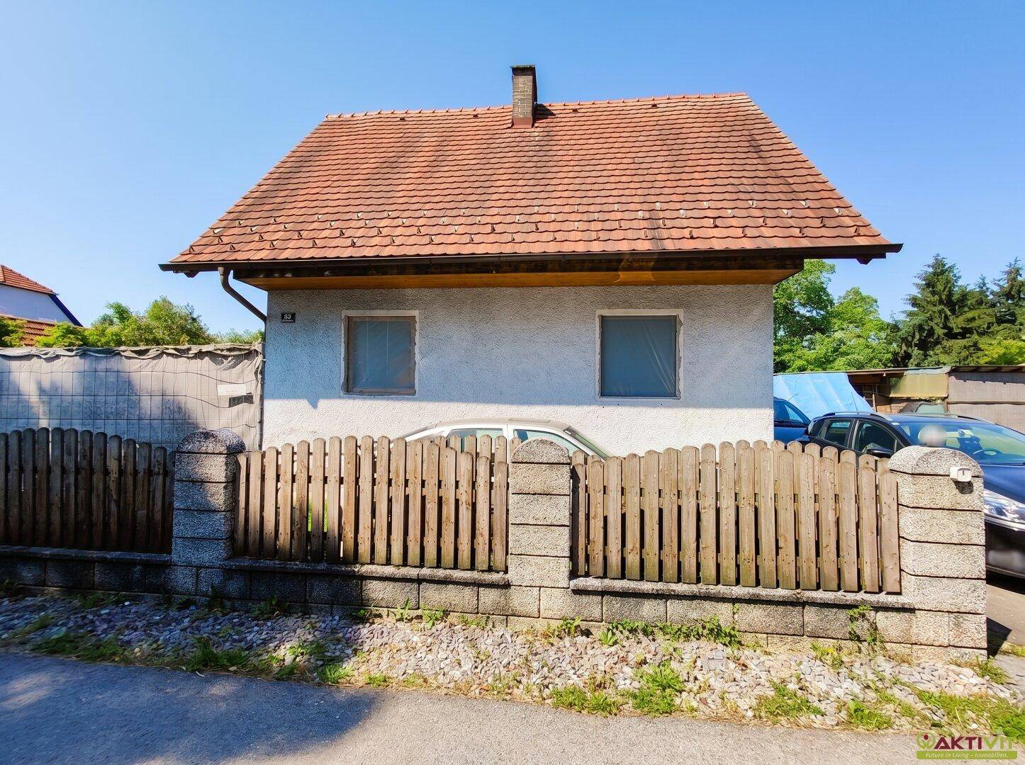 Vorderansicht eines Einfamilienhauses mit Holzzaun und Satteldach unter blauem Himmel.