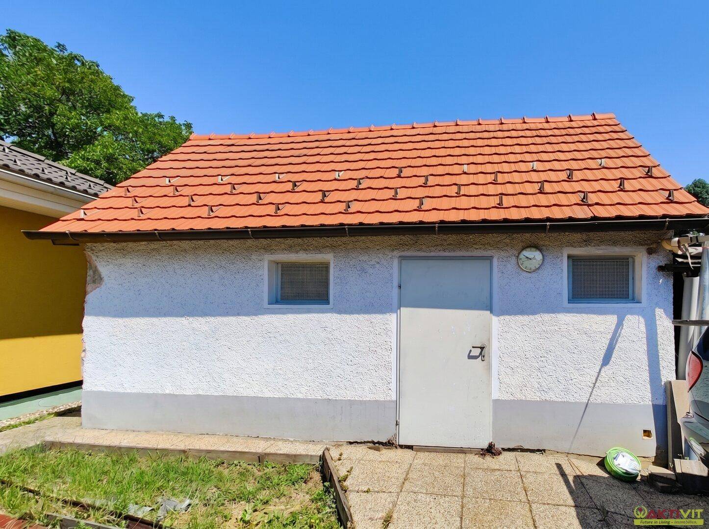 Kleines Nebengebäude mit rotem Ziegeldach und weißer Fassade im Gartenbereich.