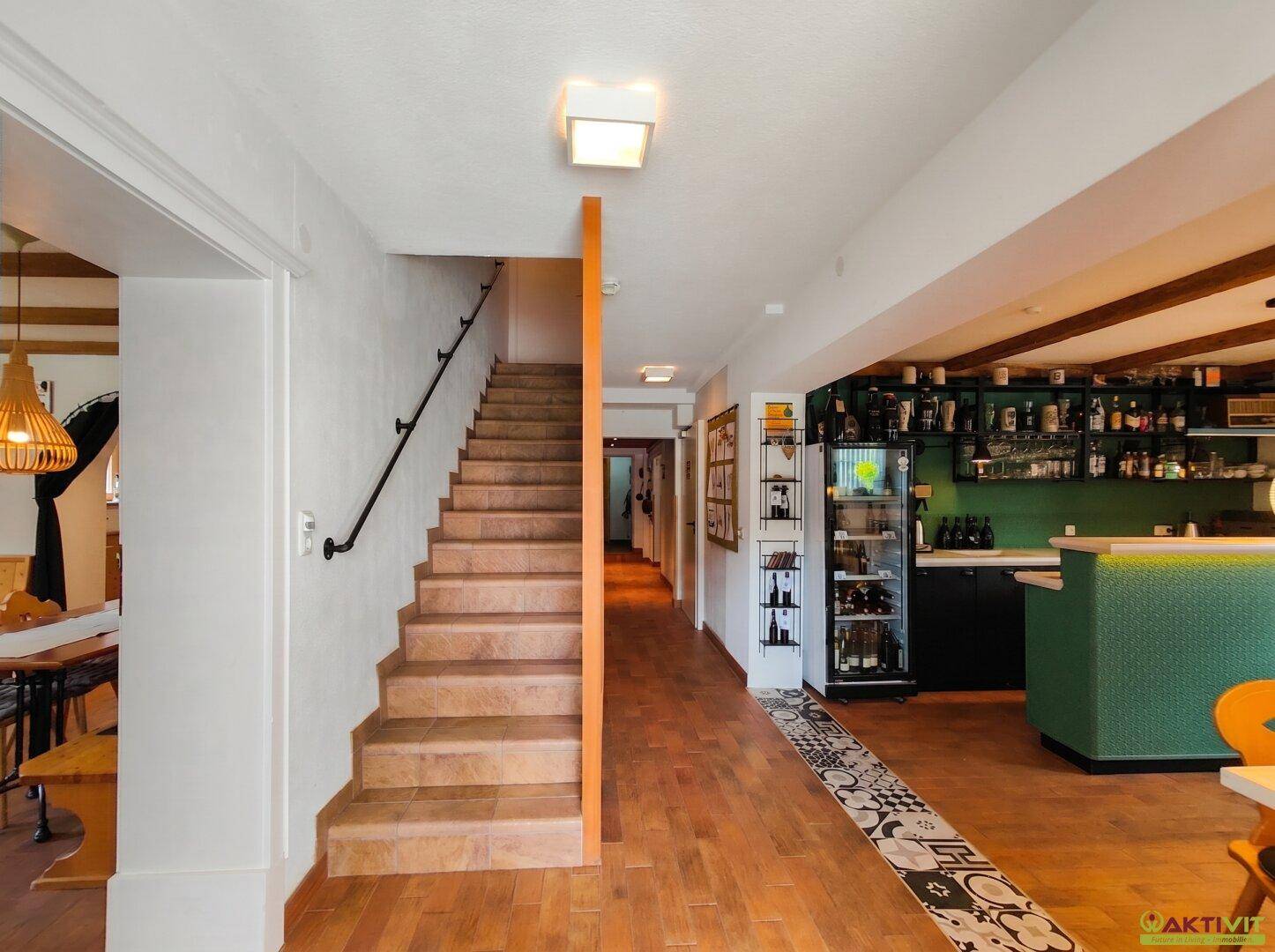 Heller Eingangsbereich mit Holztreppe, gefliestem Boden und einer modernen Bar im Hintergrund.