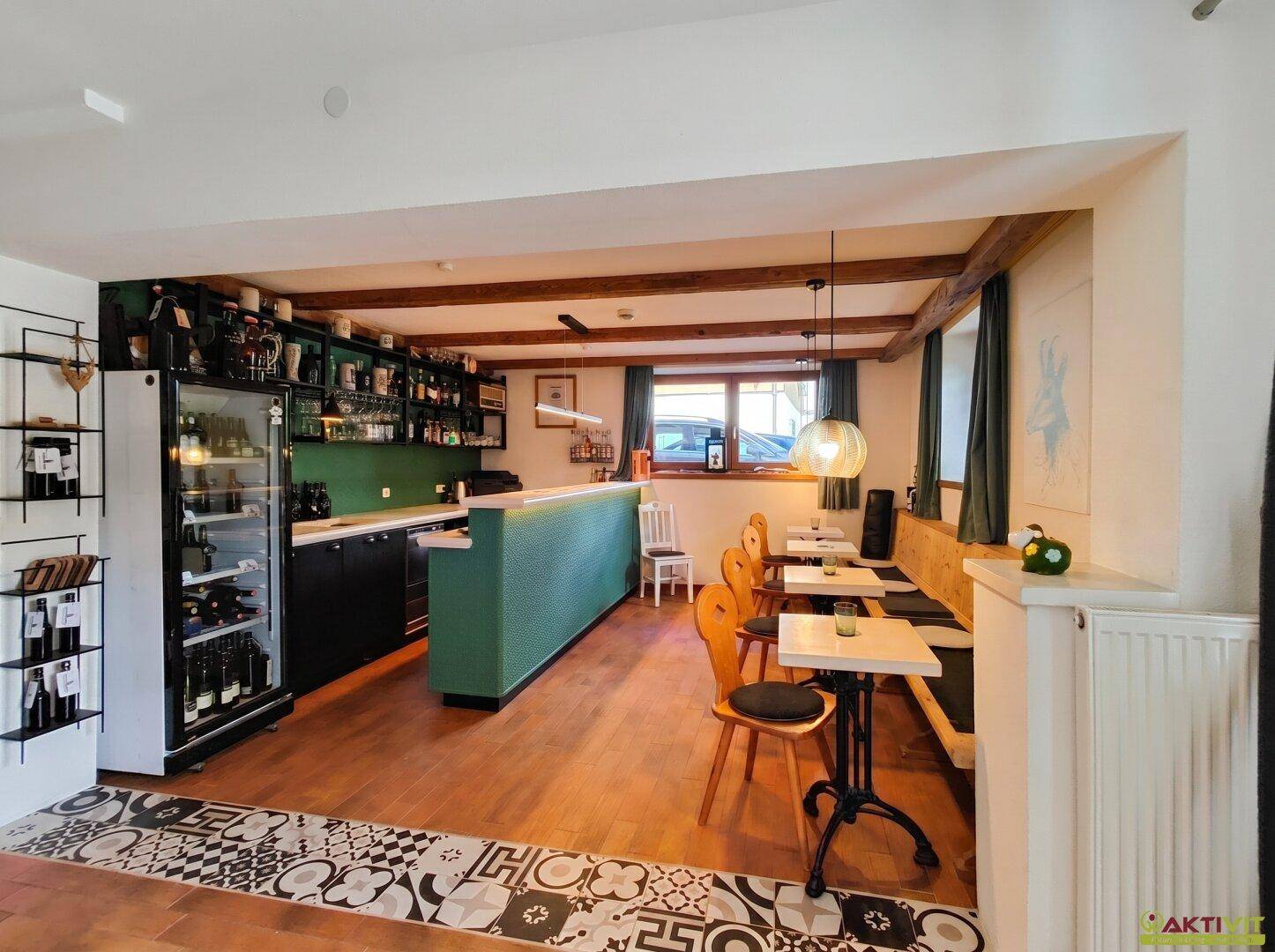 Gemütlicher Bar- und Essbereich mit Holzbalkendecke, grüner Theke und traditionellen Tischen und Stühlen.