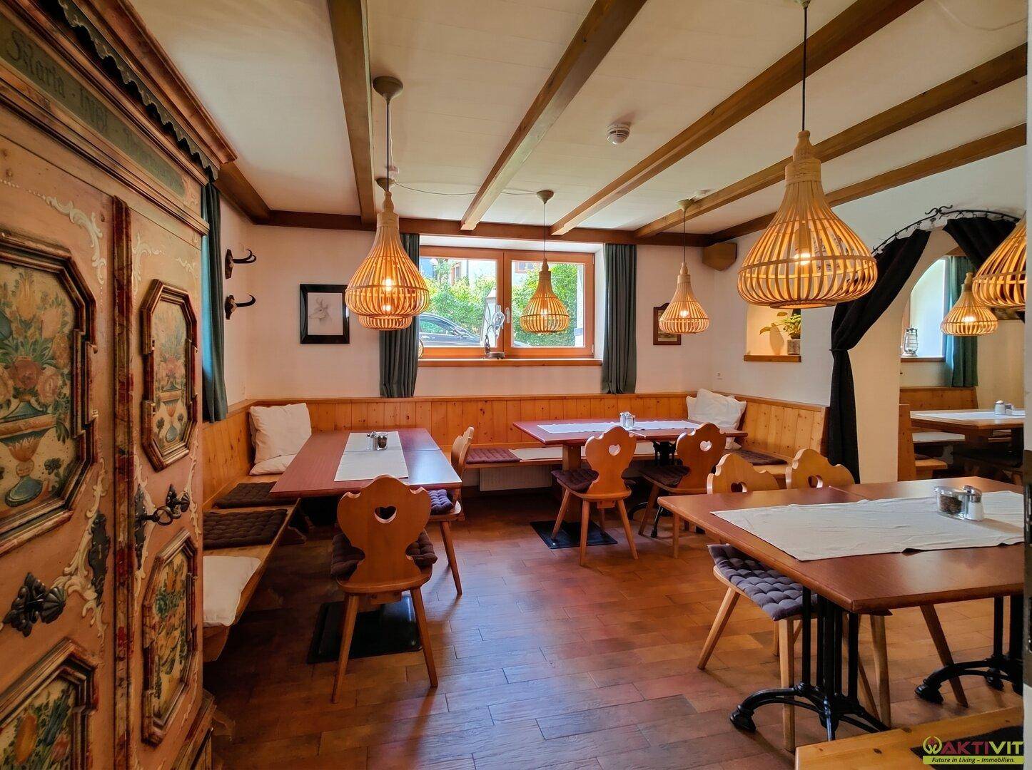 Traditioneller Speisesaal mit Holztischen, Bänken und Deckenbalken, beleuchtet von rustikalen Hängelampen.