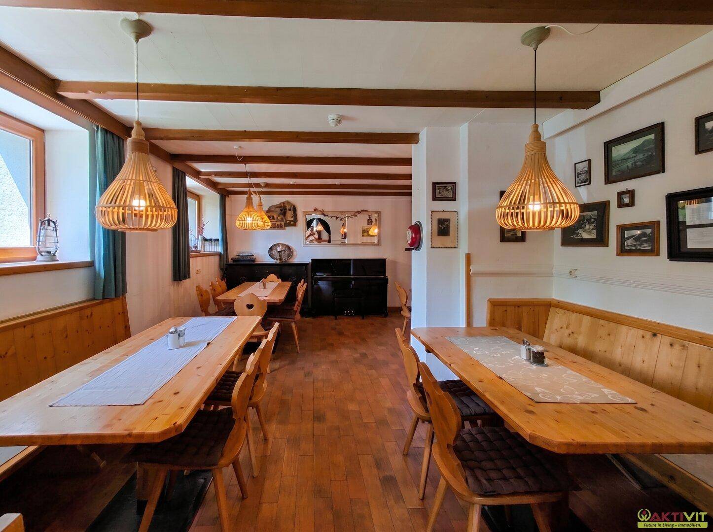 Geräumiger Speisesaal mit mehreren Holztischen, einem Klavier und traditioneller Dekoration an den Wänden.