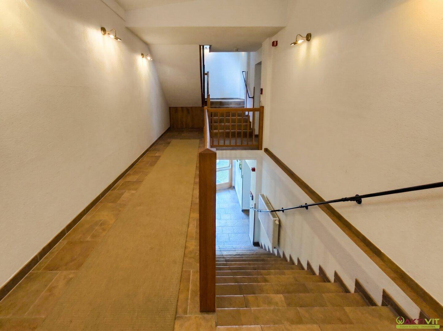 Geräumiges Treppenhaus mit gefliestem Boden und Holzgeländer, das mehrere Etagen verbindet.