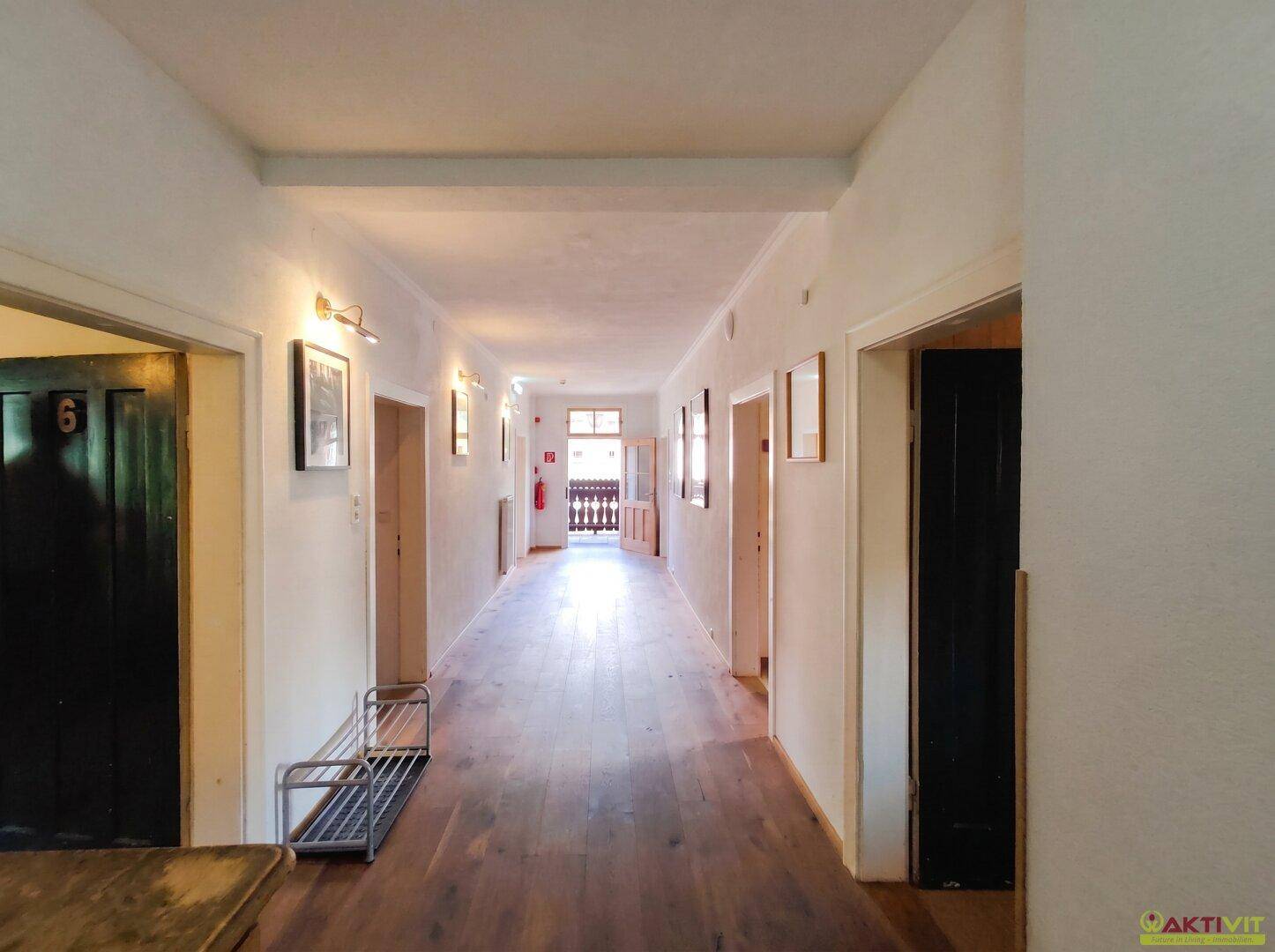 Langer Flur im Obergeschoss mit Holzboden, mehreren Türen und einem Schuhregal.