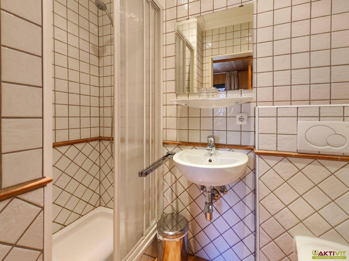 Helles Badezimmer mit weißen Fliesen, Duschkabine und Waschbecken, in gutem Zustand.