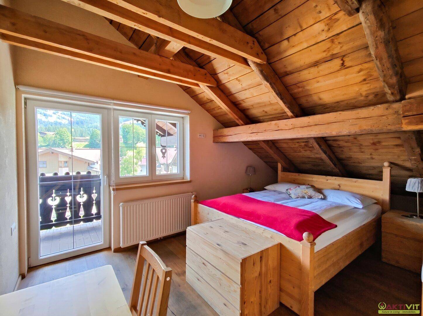 Schlafzimmer im Dachgeschoss mit Holzbalkendecke, Doppelbett und Zugang zu einem Balkon mit Bergblick.