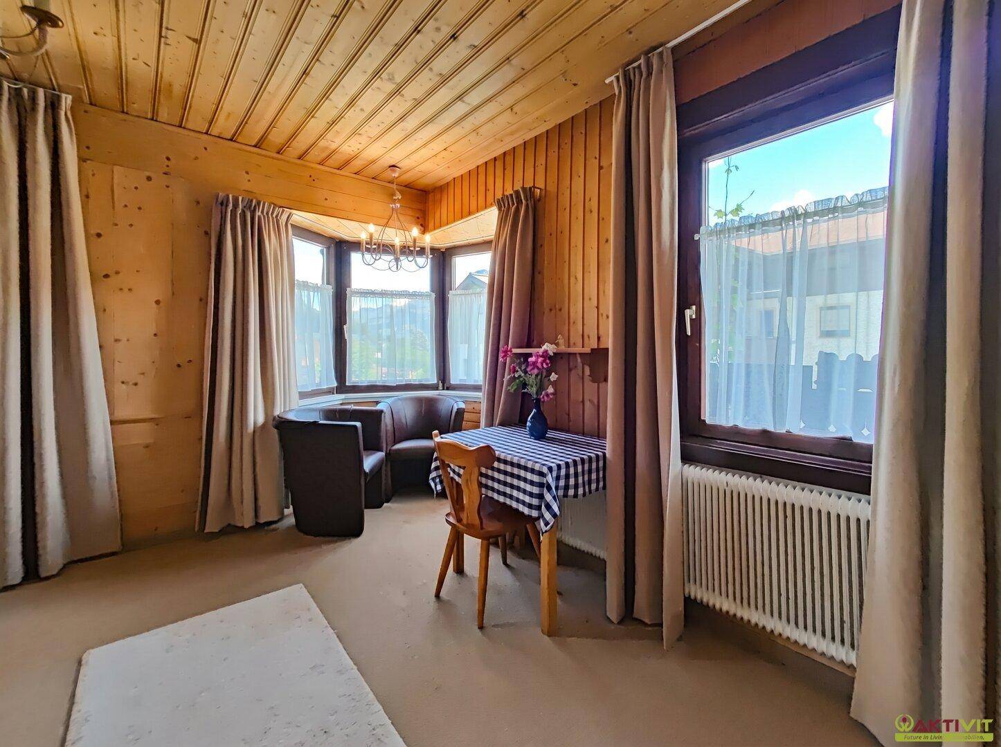 Gemütliches Wohnzimmer mit Holzwänden und -decke, Erkerfenster und bequemen Sitzgelegenheiten.