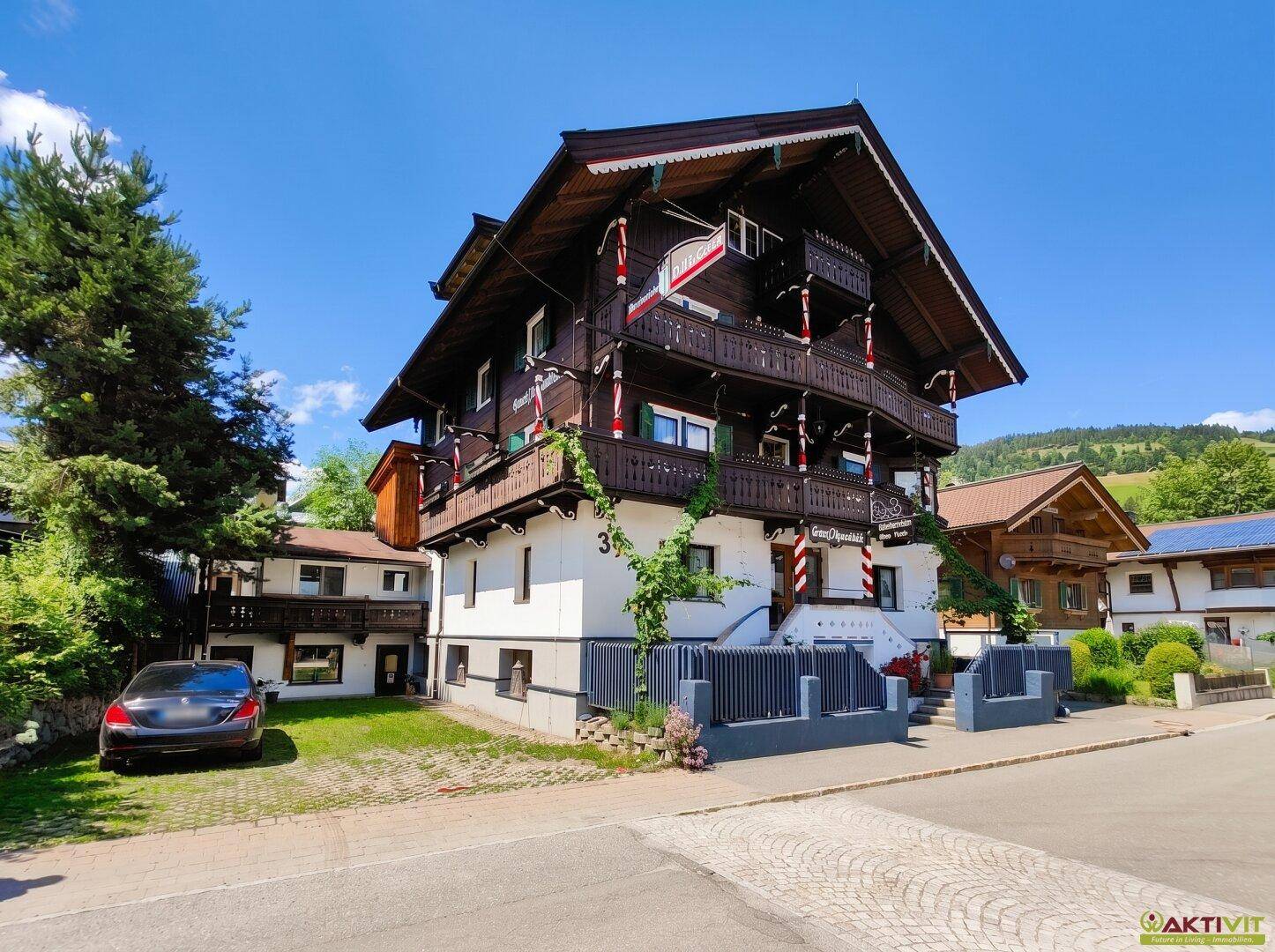 Außenansicht des traditionellen Gebäudes mit geparktem Auto und Zufahrt, umgeben von Bäumen.