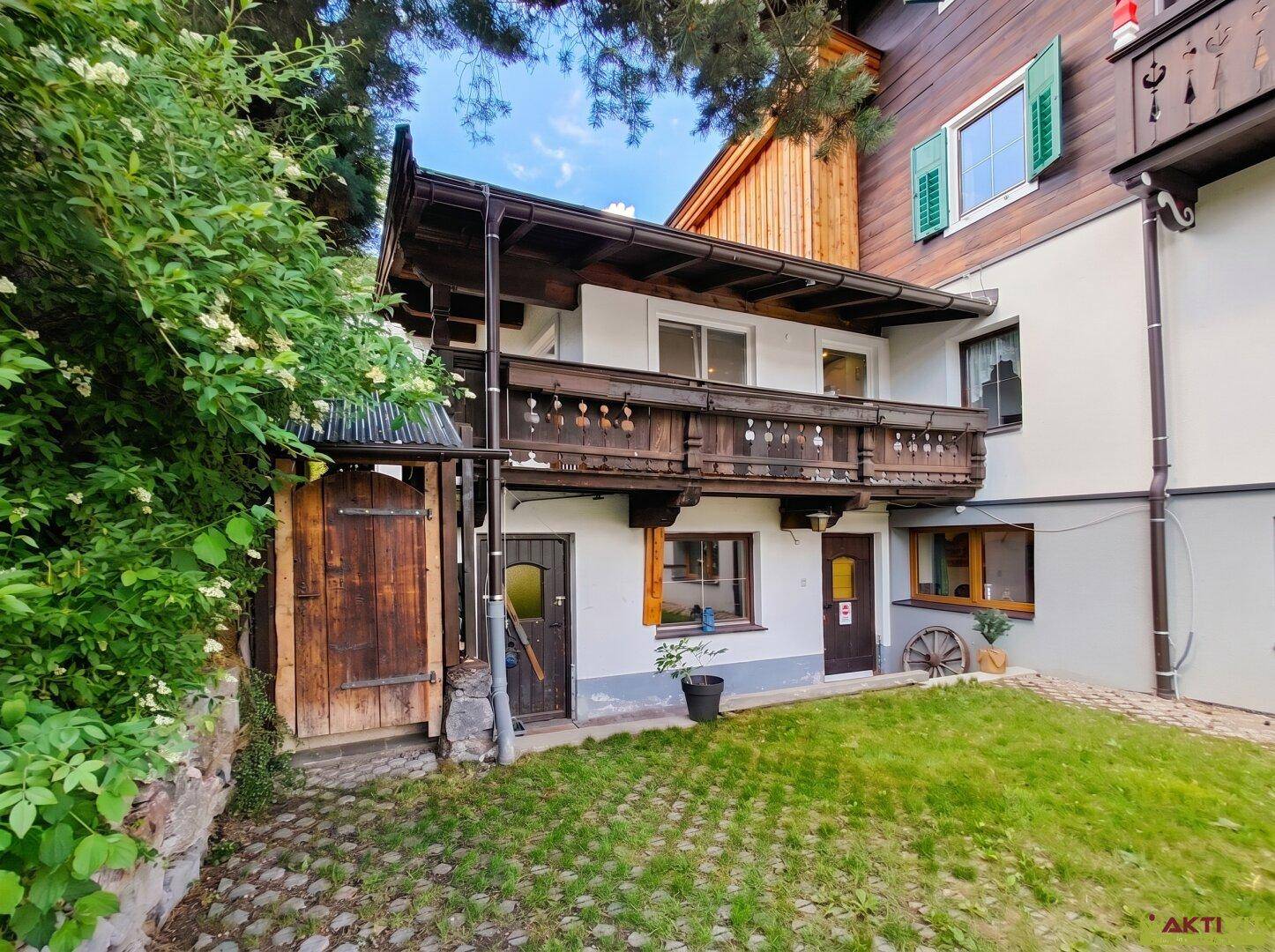 Traditionelles Haus mit Holzbalkon und grünem Gartenbereich, umgeben von Bäumen und Sträuchern.