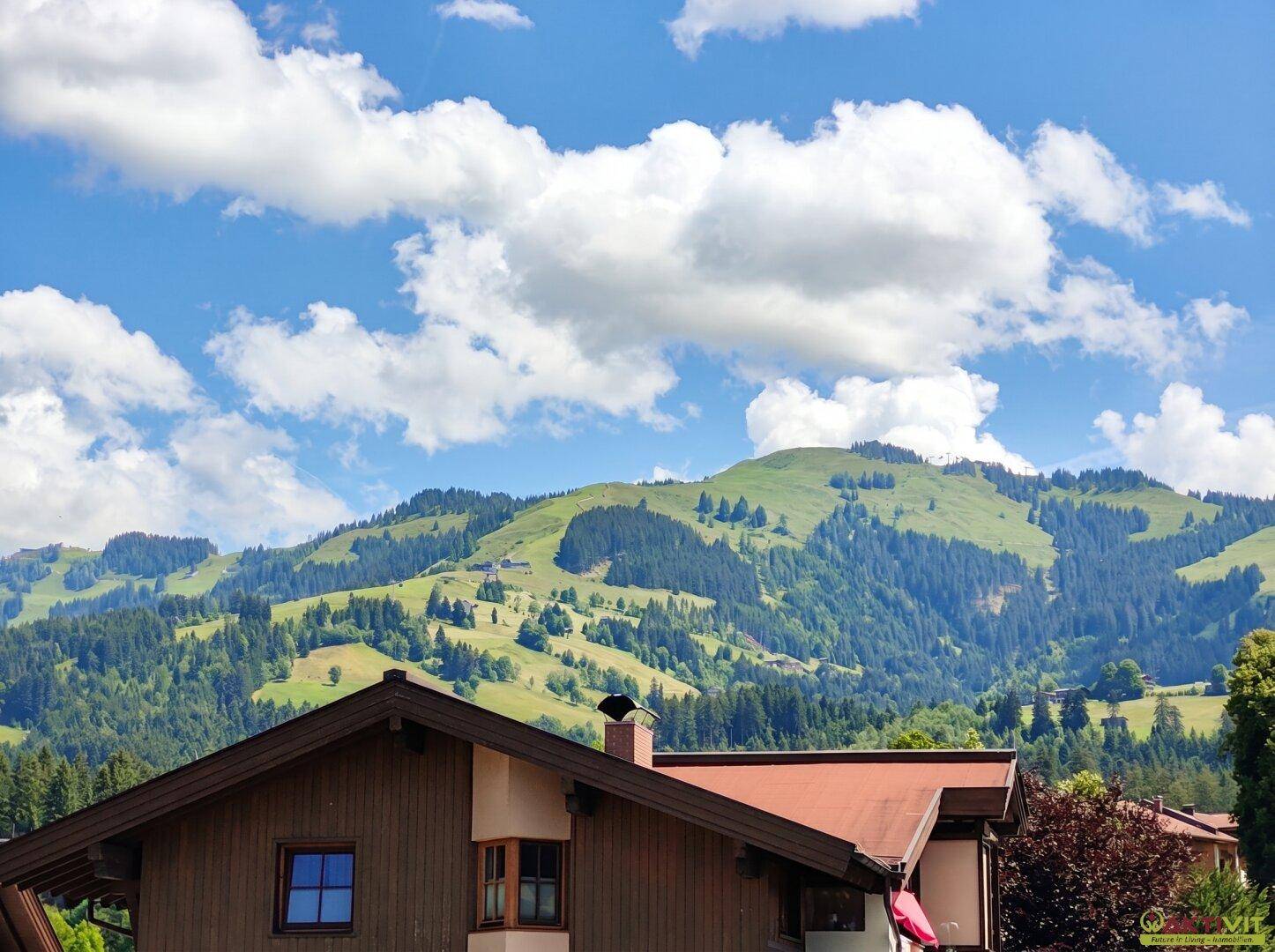 Malerischer Blick auf grüne Berge und bewaldete Hänge unter einem strahlend blauen Himmel.