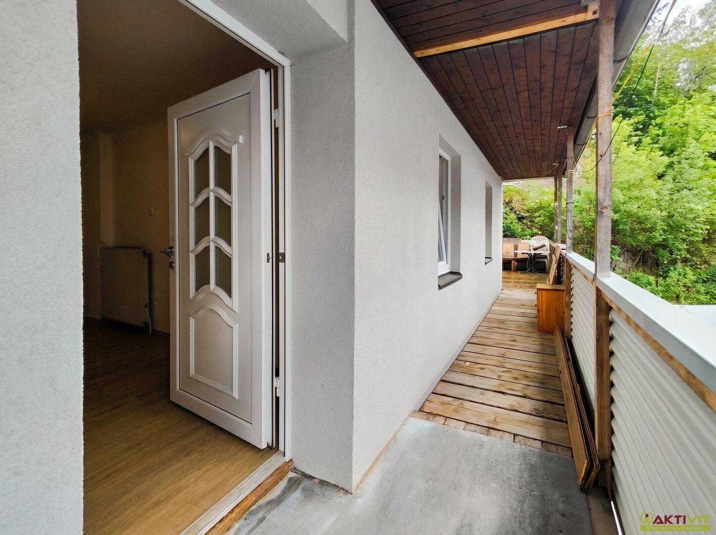 Eingangsbereich mit hellem Holzboden und Zugang zu einem überdachten Balkon mit Holzdielen.