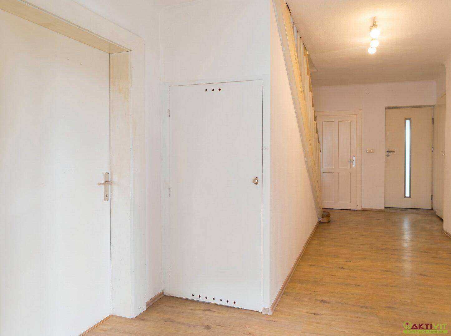 Heller Flur mit Holzboden, weiß gestrichenen Wänden und einer Holztreppe zum Obergeschoss.