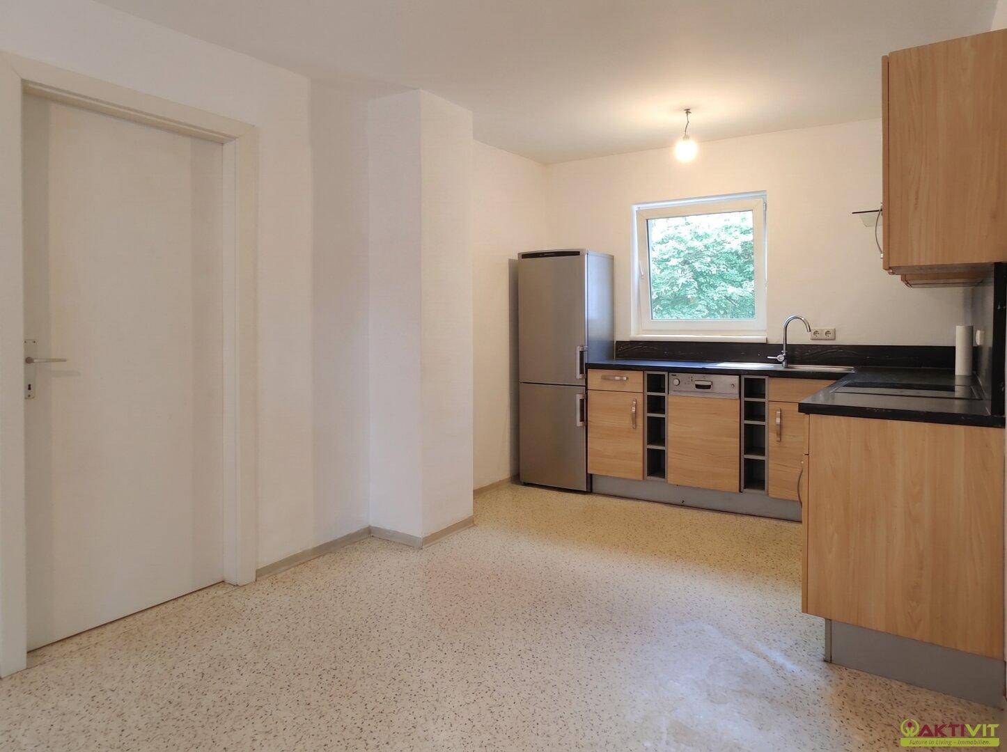 Geräumige Küche mit Holzschränken, dunkler Arbeitsplatte und ausreichend Platz für einen Essbereich.