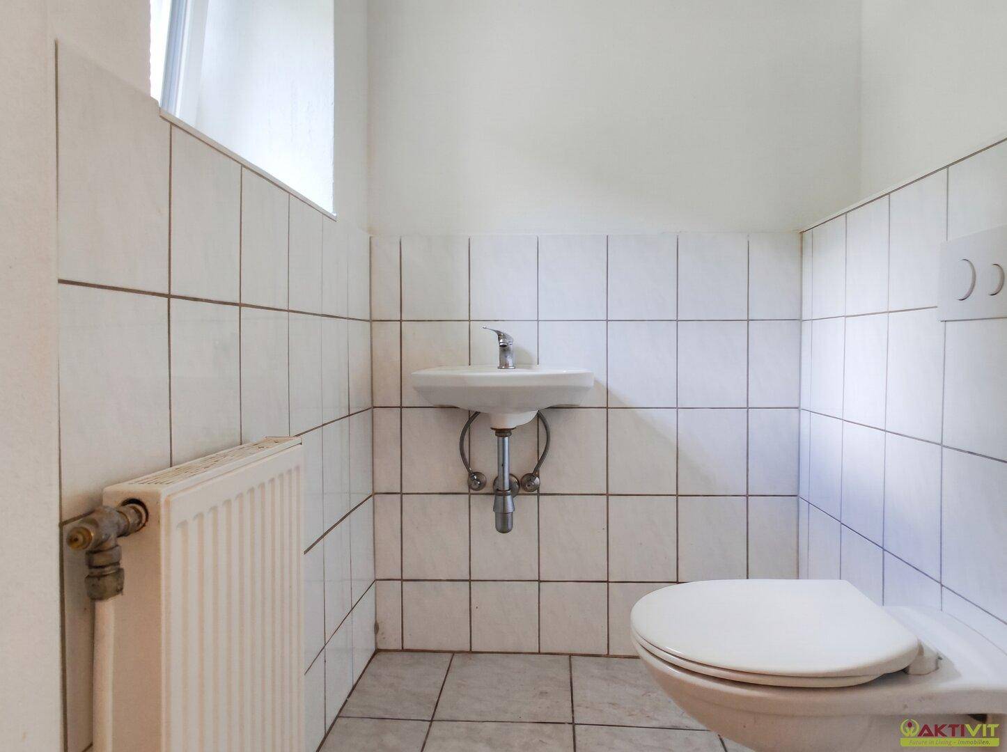Kleines Gäste-WC mit weißen Fliesen, Toilette, Waschbecken und einem Heizkörper.