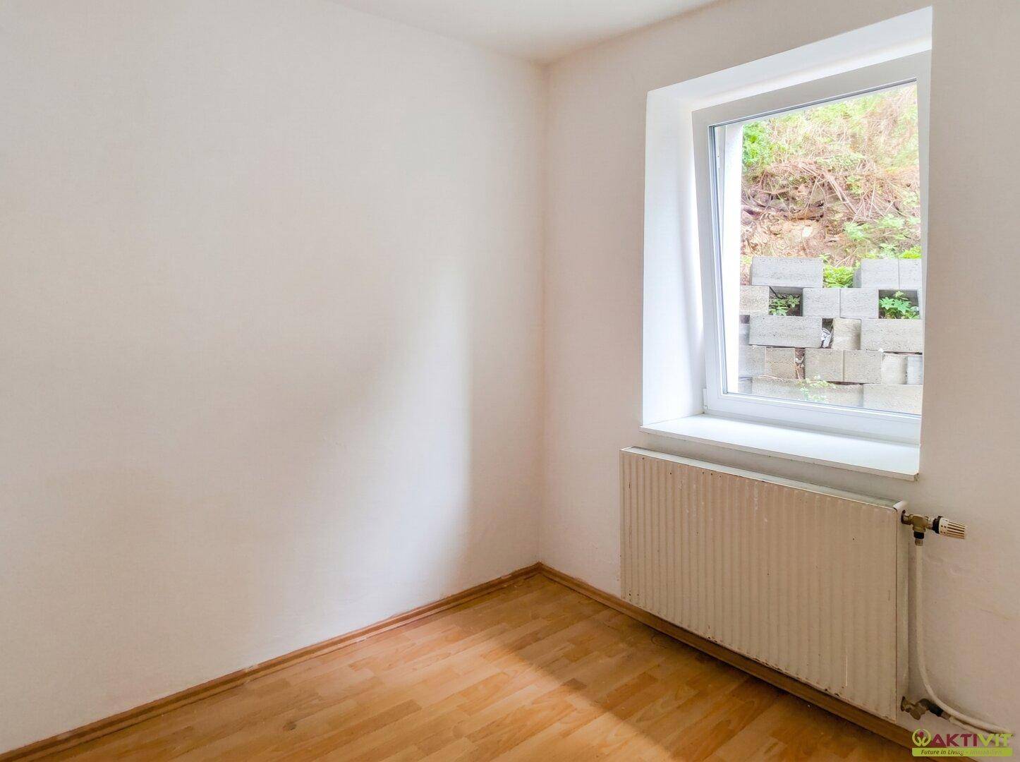 Helles Schlafzimmer mit Holzboden und einem Fenster, das einen Blick ins Grüne bietet.