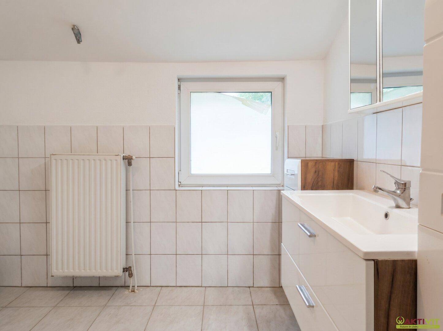 Badezimmer mit weißen Fliesen, modernem Waschbeckenunterschrank und einem Fenster.