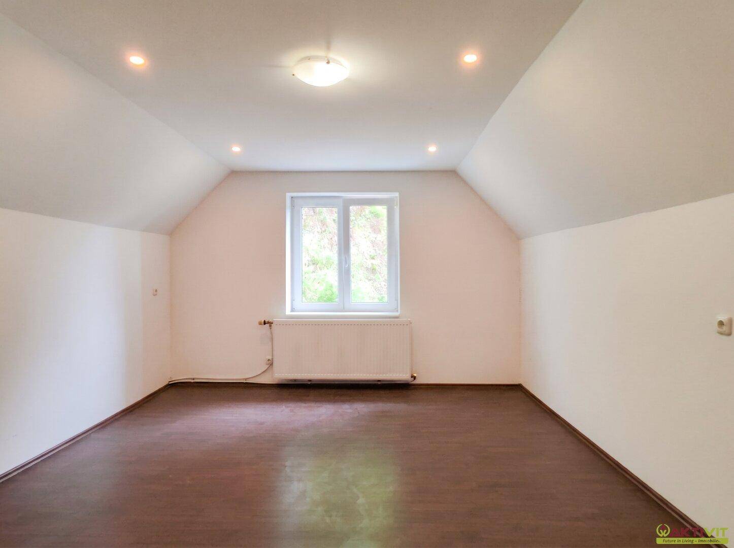 Heller Dachbodenraum mit dunklem Holzboden, schrägen Decken und einem Fenster.