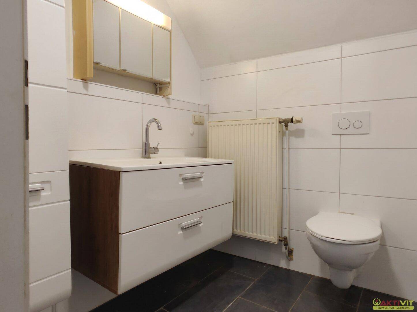 Modernes Badezimmer mit dunklen Bodenfliesen, Waschbeckenunterschrank und wandhängender Toilette.