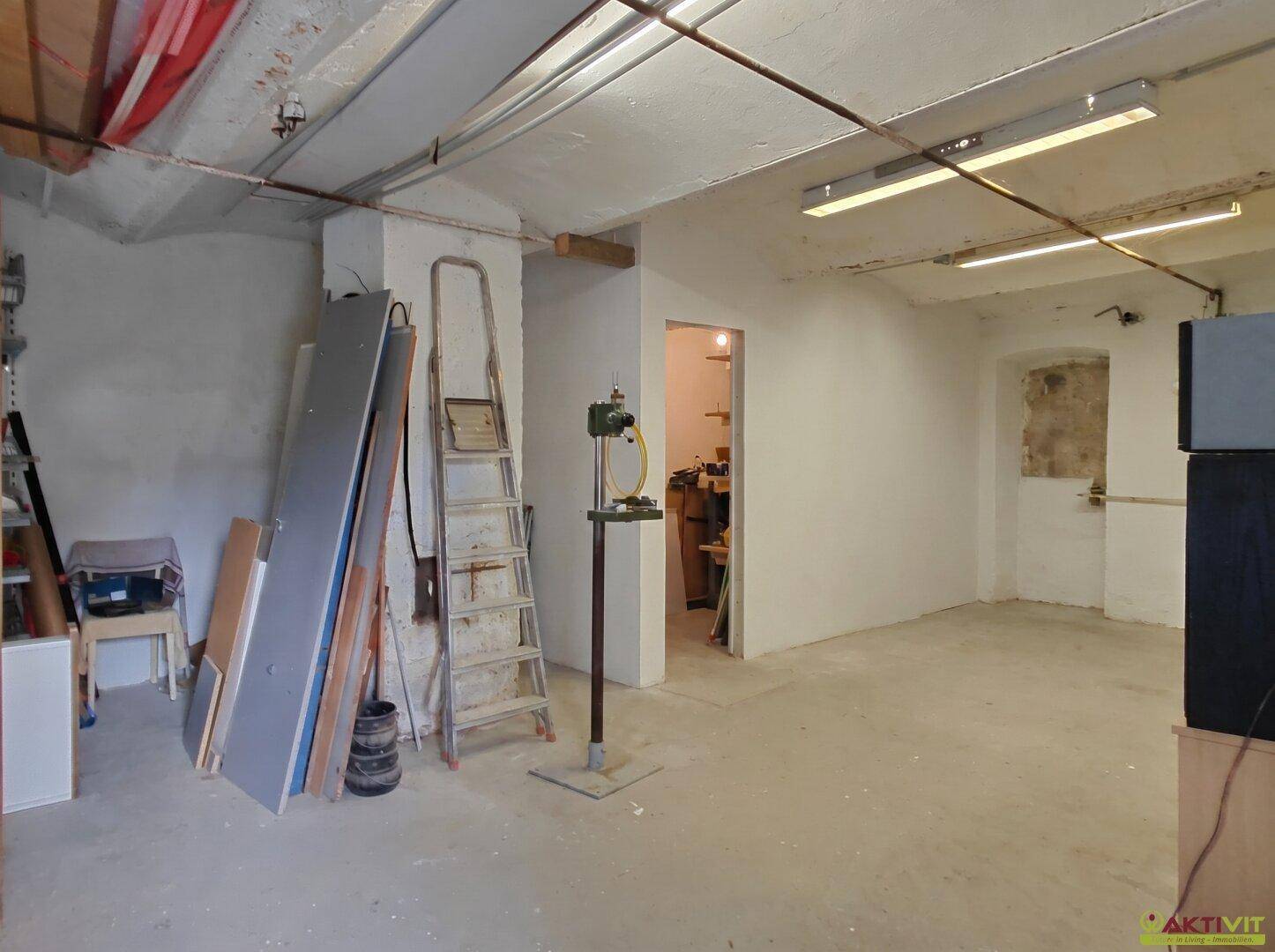 Unfertiger Kellerraum mit Betonboden, sichtbaren Rohren und einer Leiter.