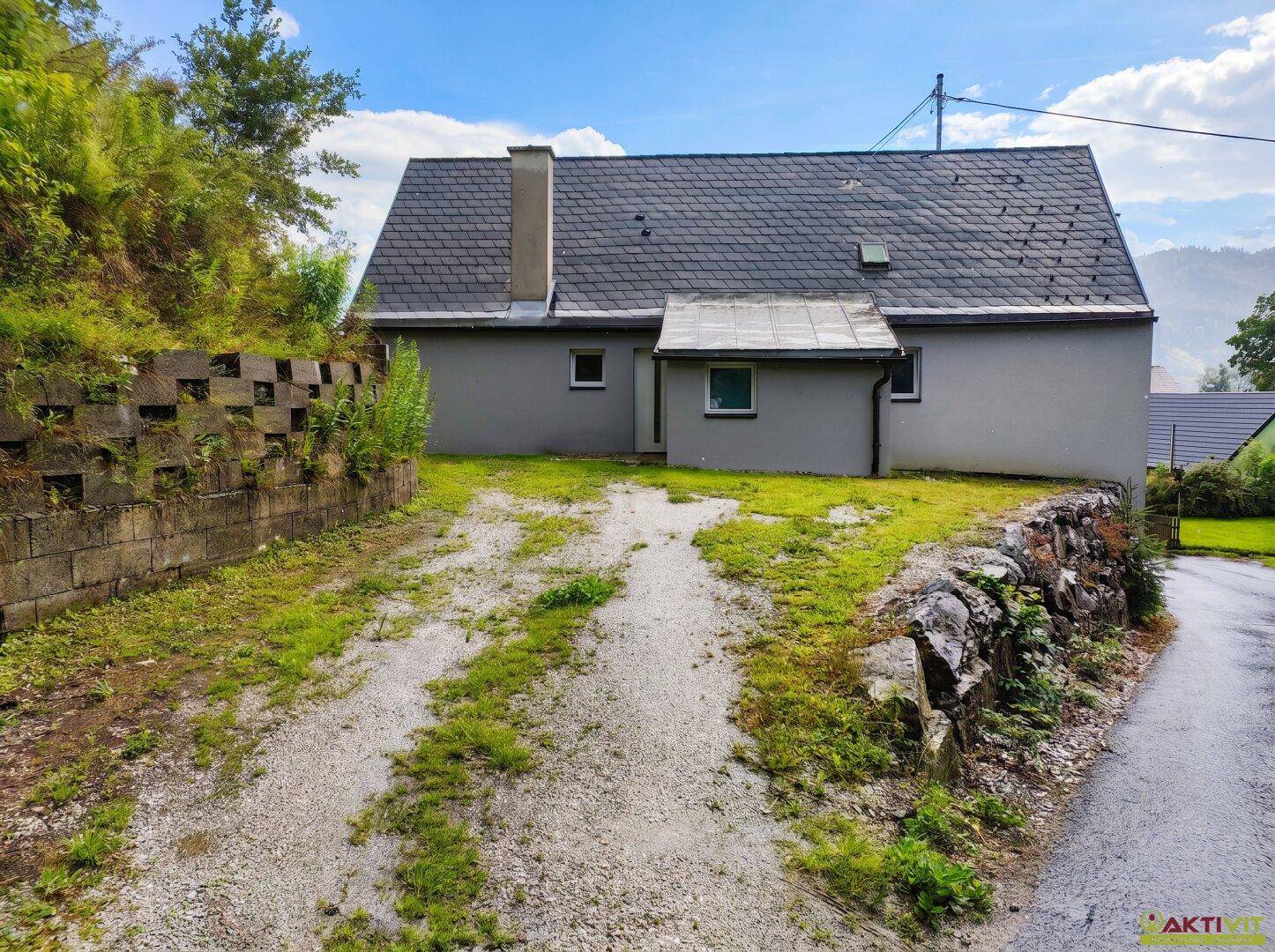 Rückansicht des Hauses mit Gartenbereich, Schotterweg und einer gemauerten Stützmauer.
