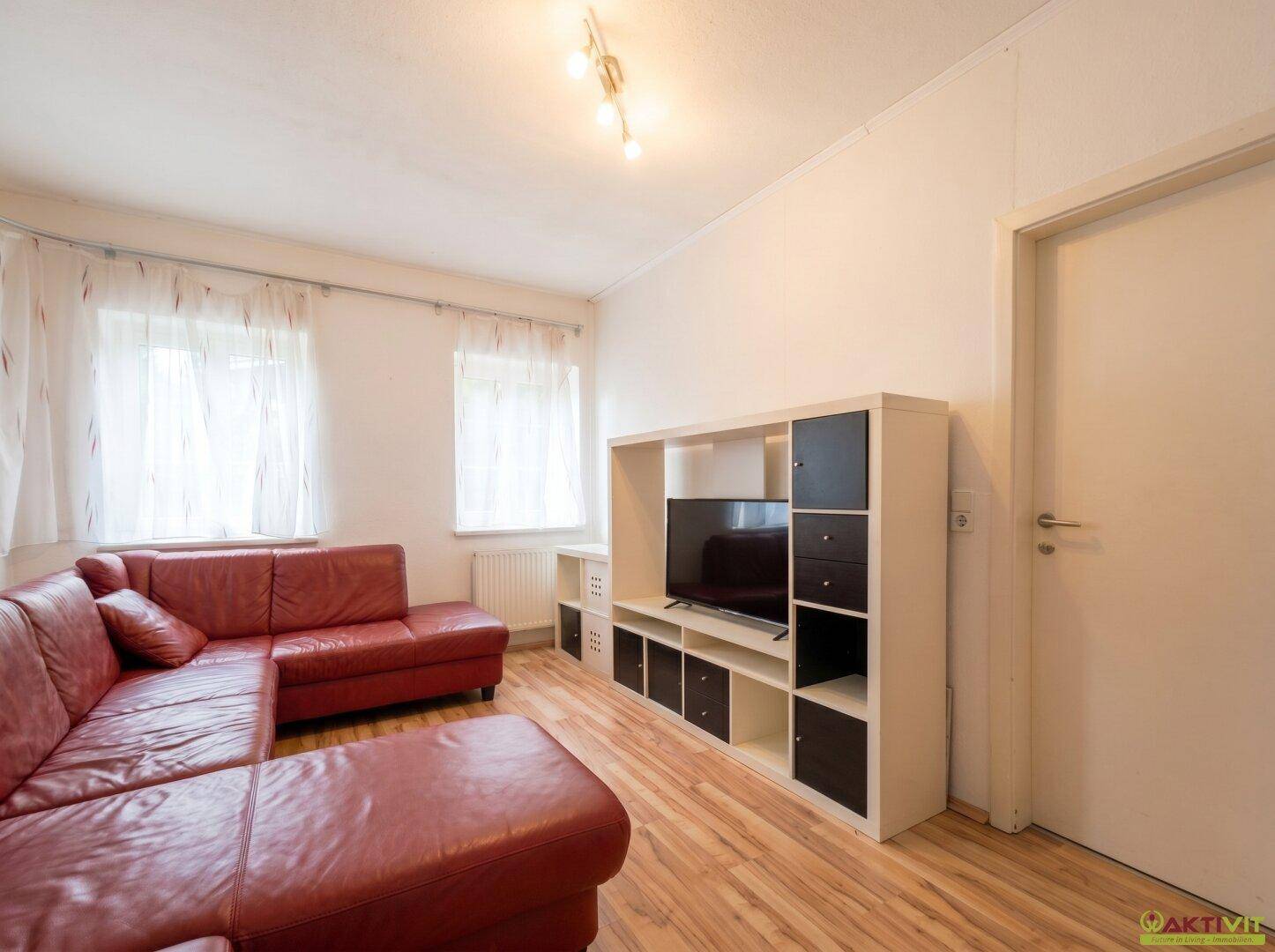 Gemütliches Wohnzimmer mit rotem Ledersofa, TV-Möbel und Laminatboden.