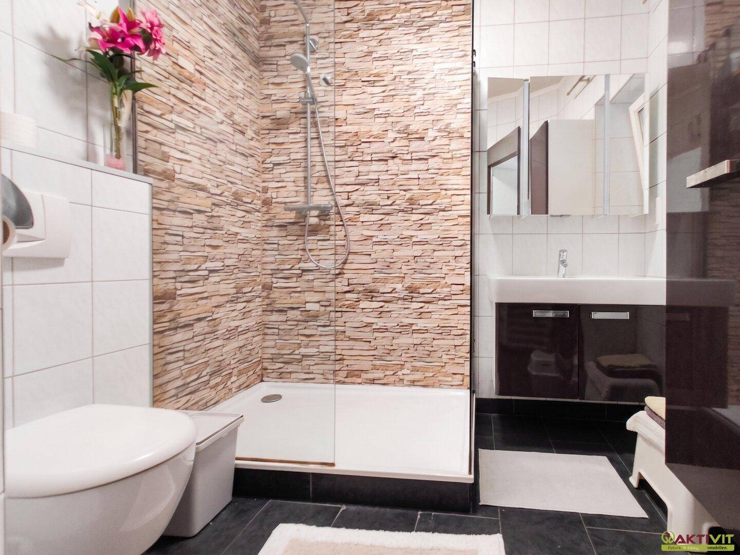 Modernes Badezimmer mit begehbarer Dusche, Steinwandfliesen und dunklem Boden.