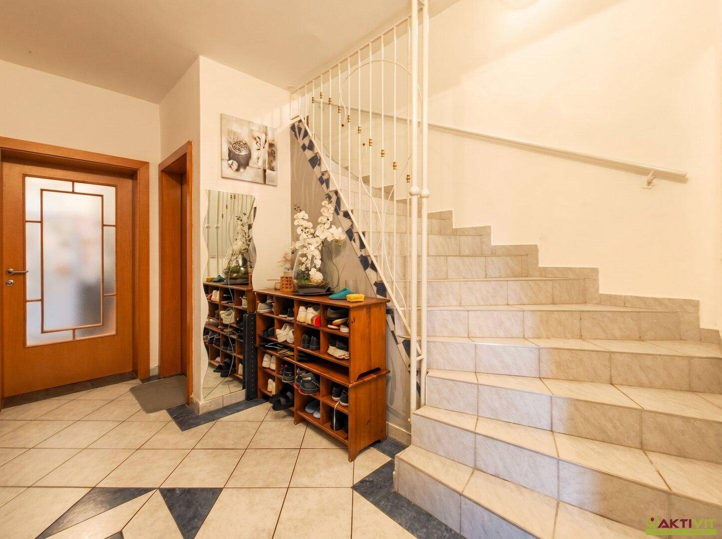 Eingangsbereich mit gefliestem Boden, Schuhregal und Treppe zum Obergeschoss.
