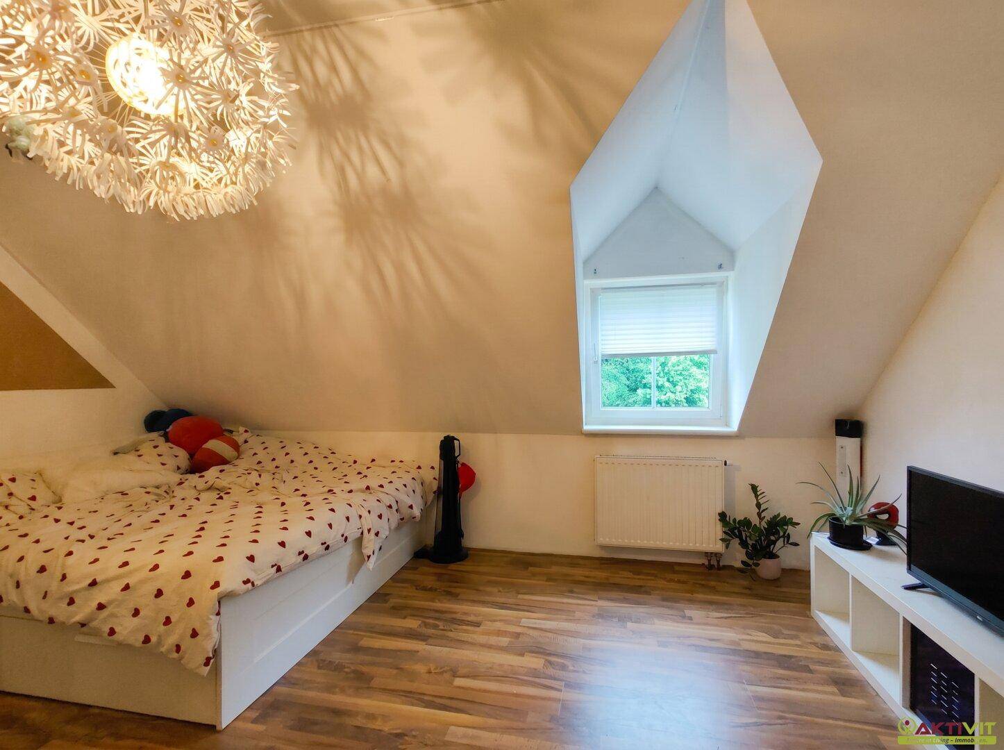 Gemütliches Schlafzimmer im Dachgeschoss mit Bett, TV und schrägen Wänden.