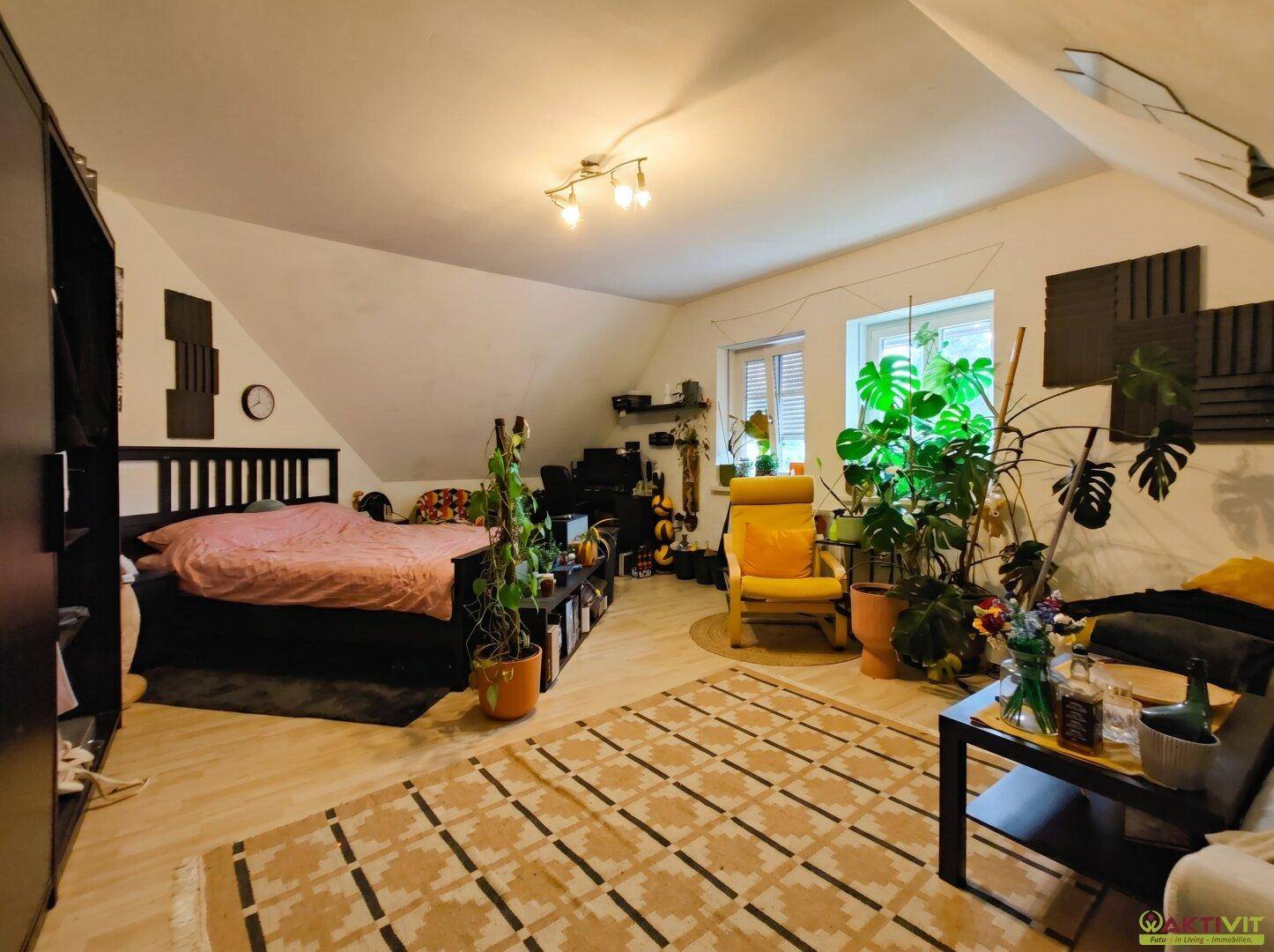 Großes Schlafzimmer im Dachgeschoss mit vielen Pflanzen, Teppich und Holzboden.