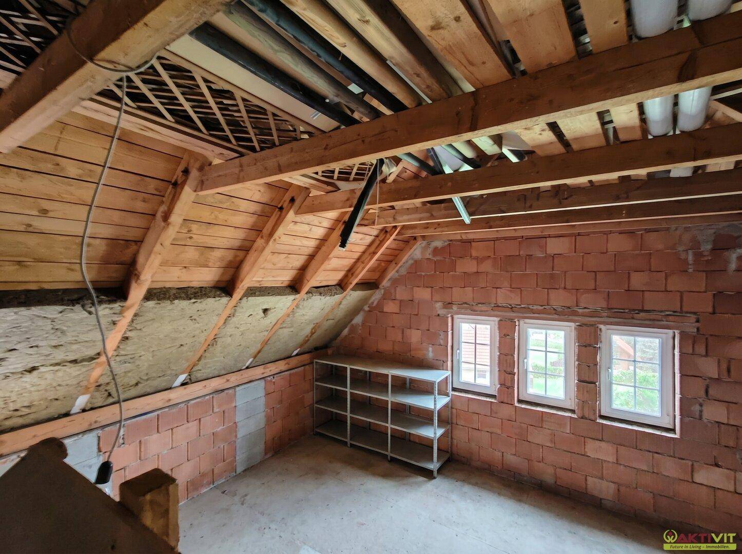 Unausgebauter Dachboden mit Holzbalken, Ziegelwänden und Regalen, bietet Stauraum.