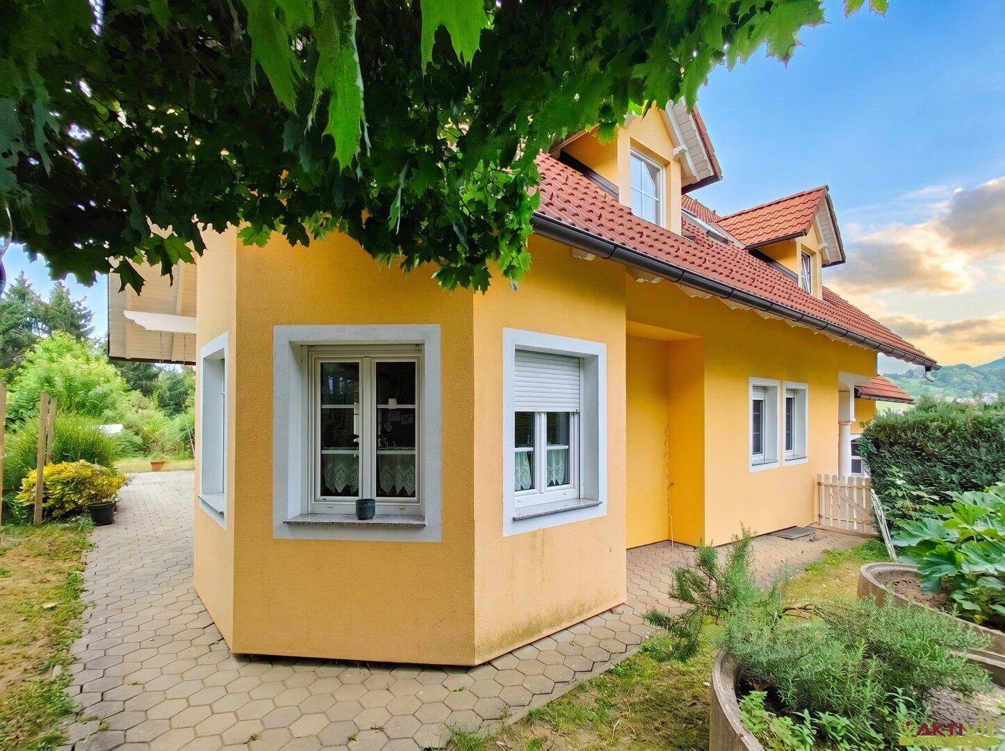 Seitenansicht des Hauses mit Garten, Hochbeeten und grüner Bepflanzung.