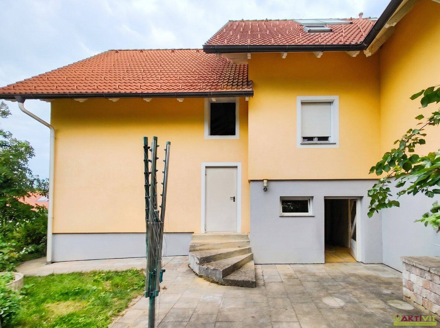 Rückseite des Hauses mit gepflasterter Terrasse, Außentreppe und Zugang zum Kellerbereich.