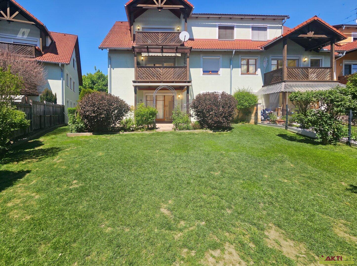 Gepflegter Gartenbereich mit Rasenfläche und Zugang zum Haus mit Balkonen und Terrasse.