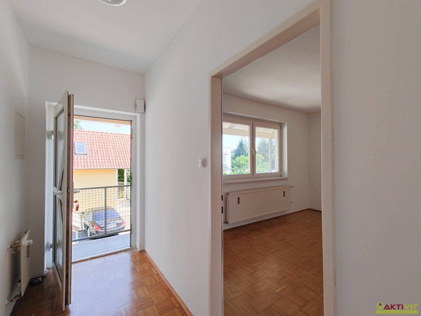 Eingangsbereich mit Parkettboden und Zugang zu einem kleinen Balkon mit Blick auf Dächer.