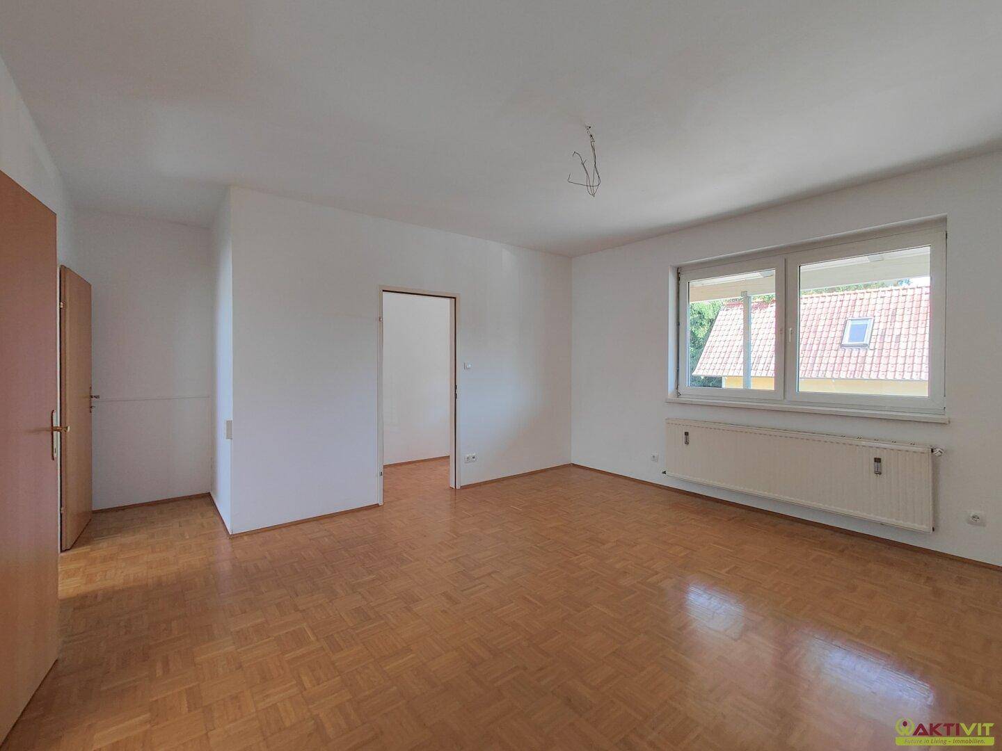 Heller Wohnraum mit Parkettboden, weißen Wänden und Blick auf ein Dachfenster.