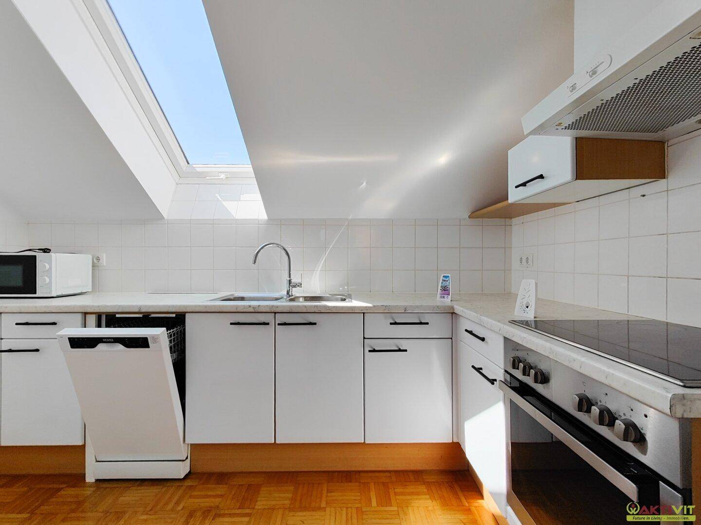Moderne Küche mit weißen Schränken, Induktionskochfeld und großem Dachfenster für viel Licht.