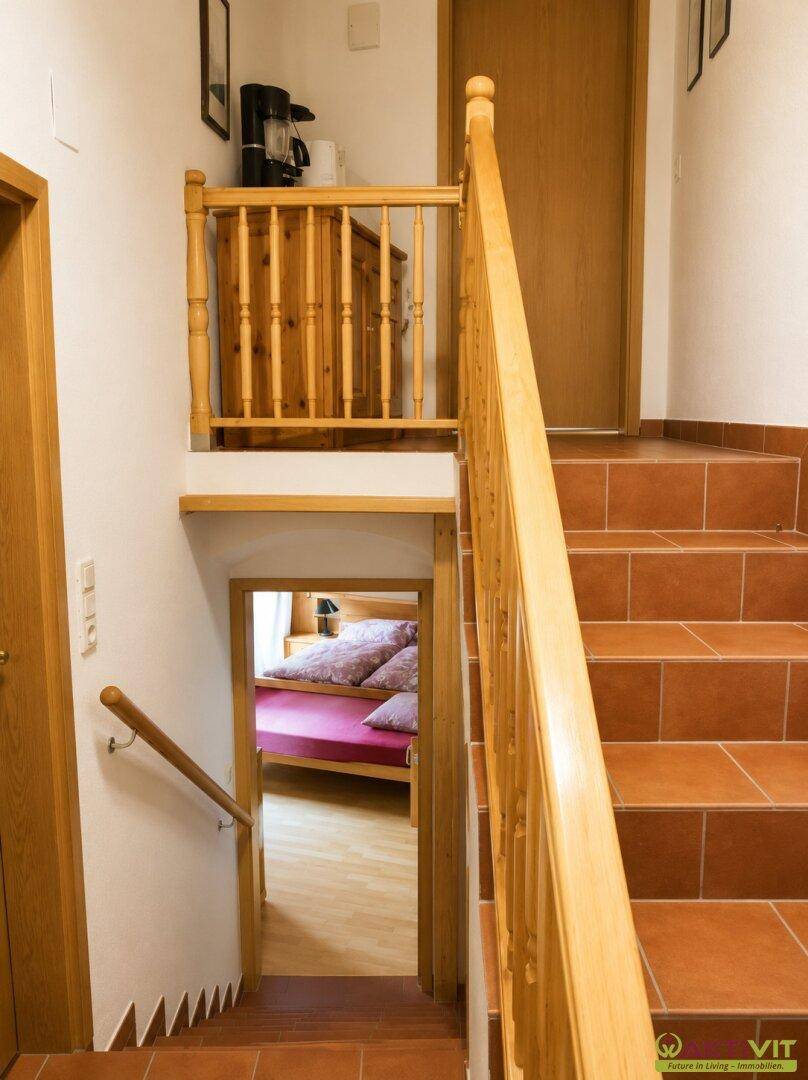 Treppenhaus mit Holzgeländer und Terrakottafliesen, das zu den oberen Etagen führt.