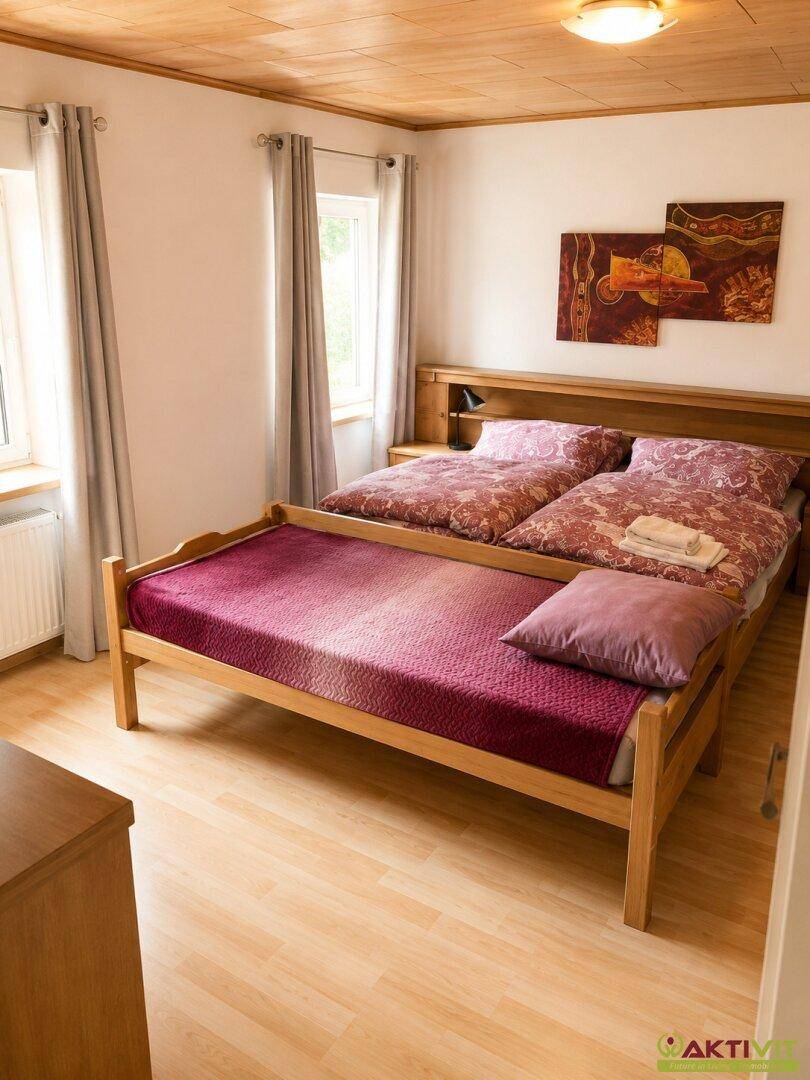 Schlafzimmer mit Doppelbett, Holzrahmen und Holzboden unter einer Holzdecke.