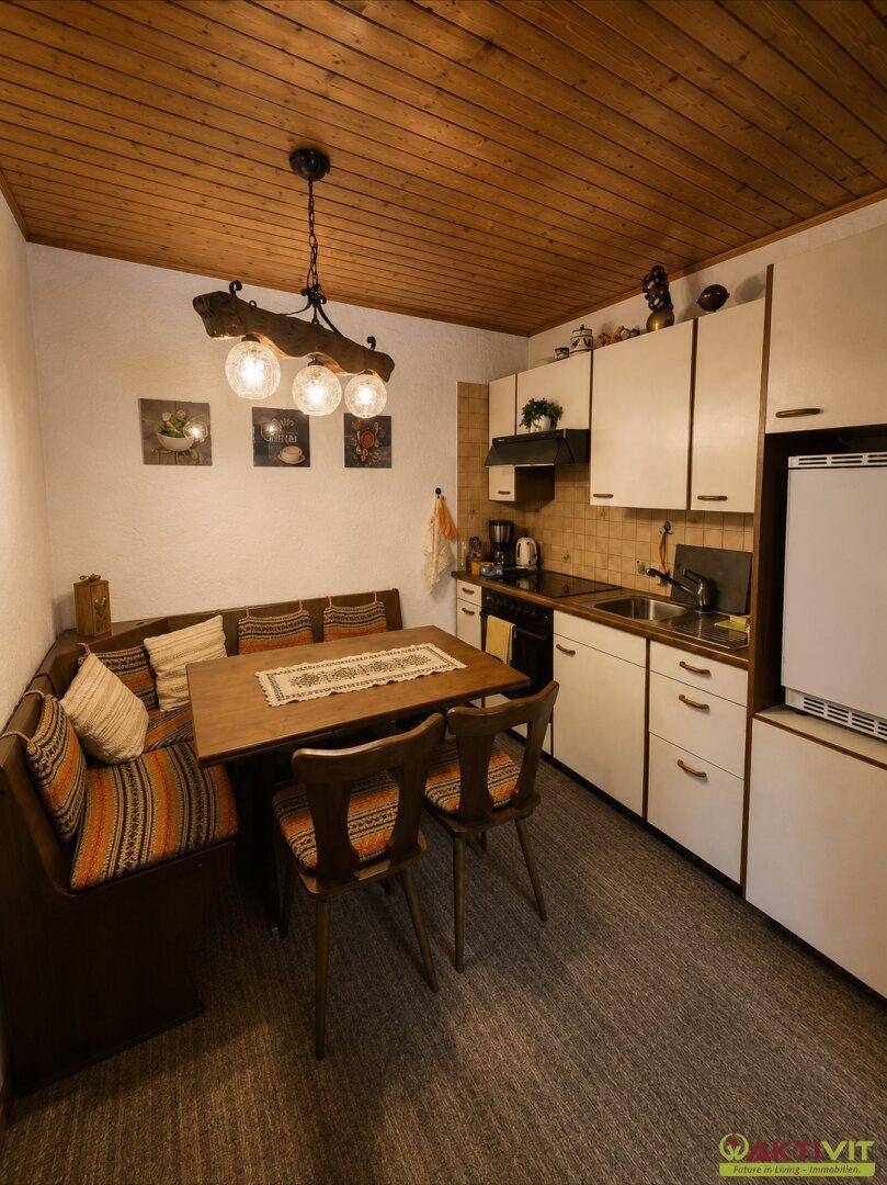 Gemütliche Wohnküche mit Eckbank, Holztisch und weißen Schränken unter einer Holzdecke.