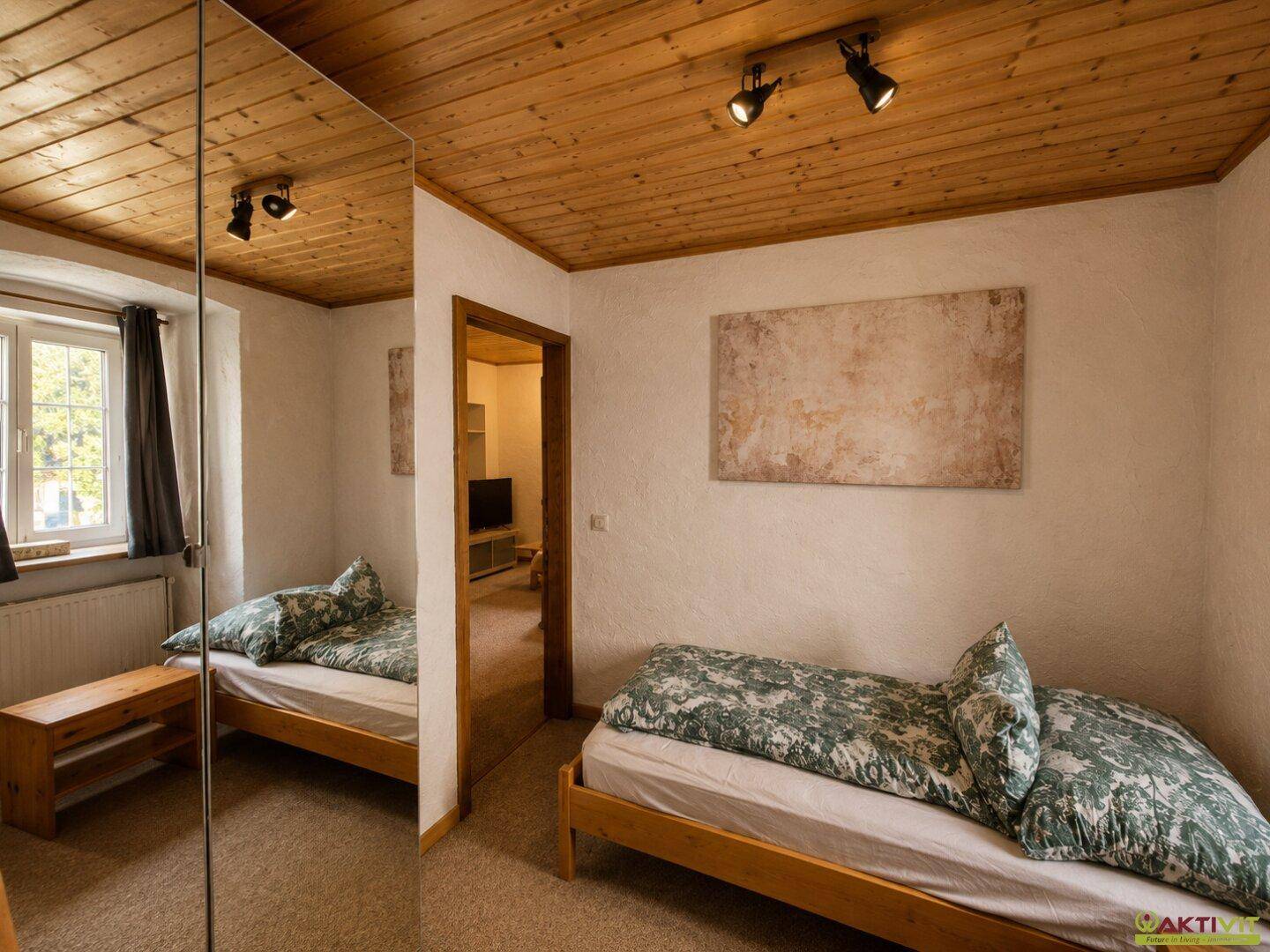 Schlafzimmer mit Einzelbett, Spiegelwand und Holzdecke.