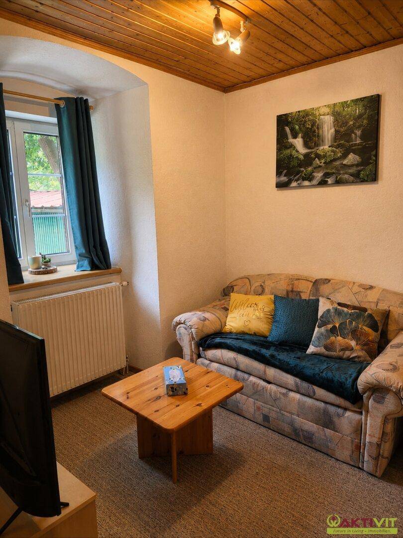 Kleines Wohnzimmer mit Sofa, Couchtisch und Blick aus dem Fenster.