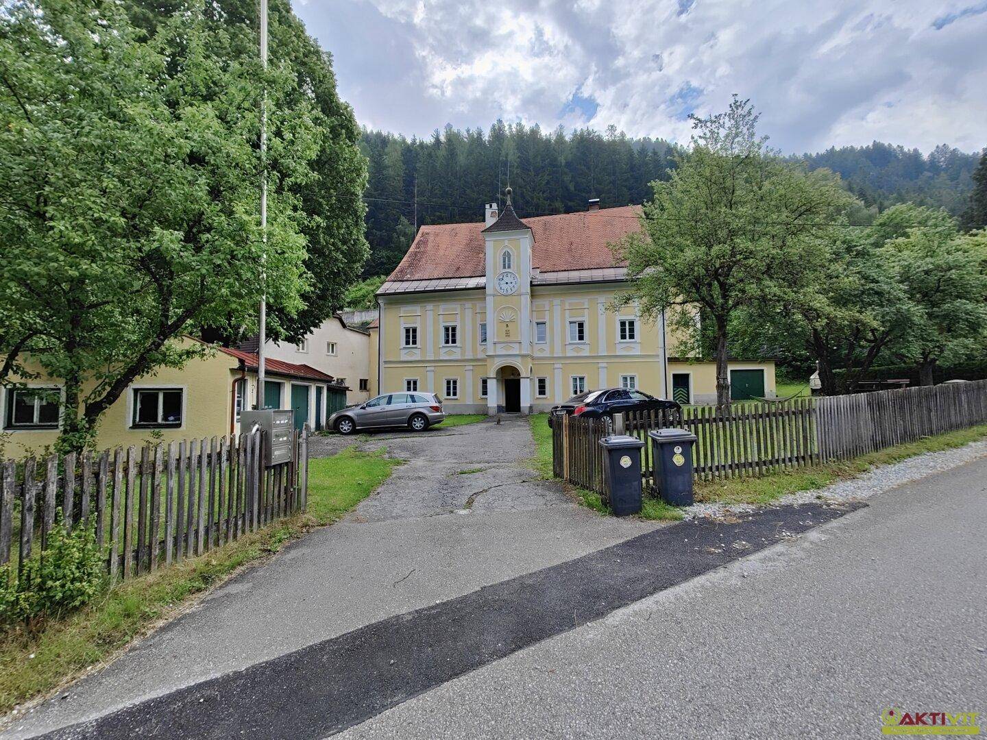 Historisches Anwesen mit gelber Fassade, Uhrturm und Zufahrt, umgeben von Bäumen.