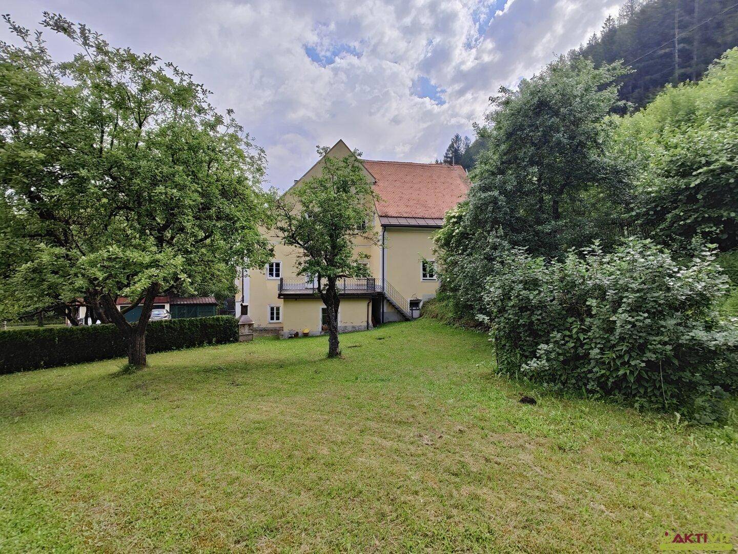 Rückansicht des historischen Gebäudes mit Garten und altem Baumbestand.