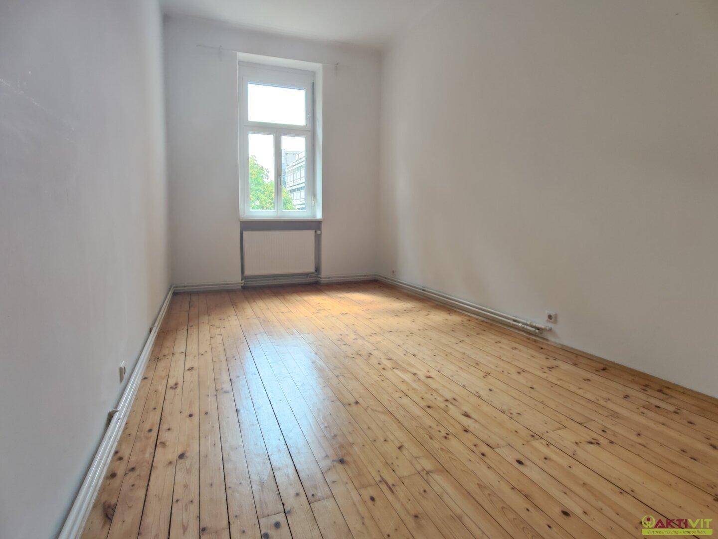 Ruhiges, helles Schlafzimmer mit Holzdielenboden und einem Fenster, das Tageslicht spendet.