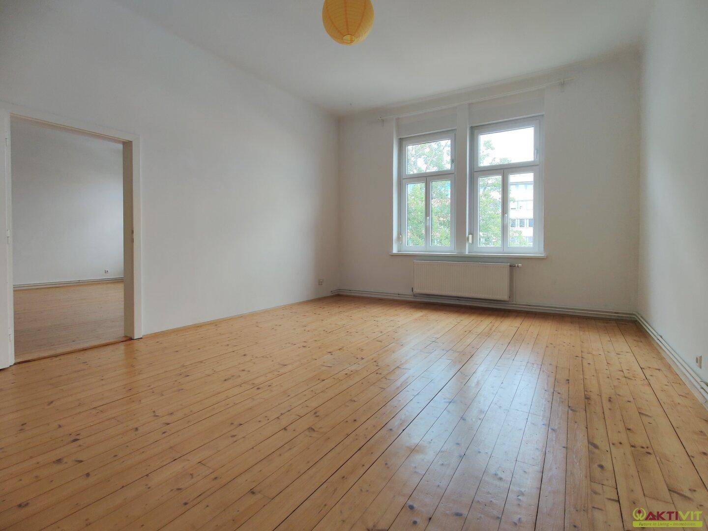 Geräumiges, helles Zimmer mit Holzdielenboden und Blick ins Grüne durch die Fenster.