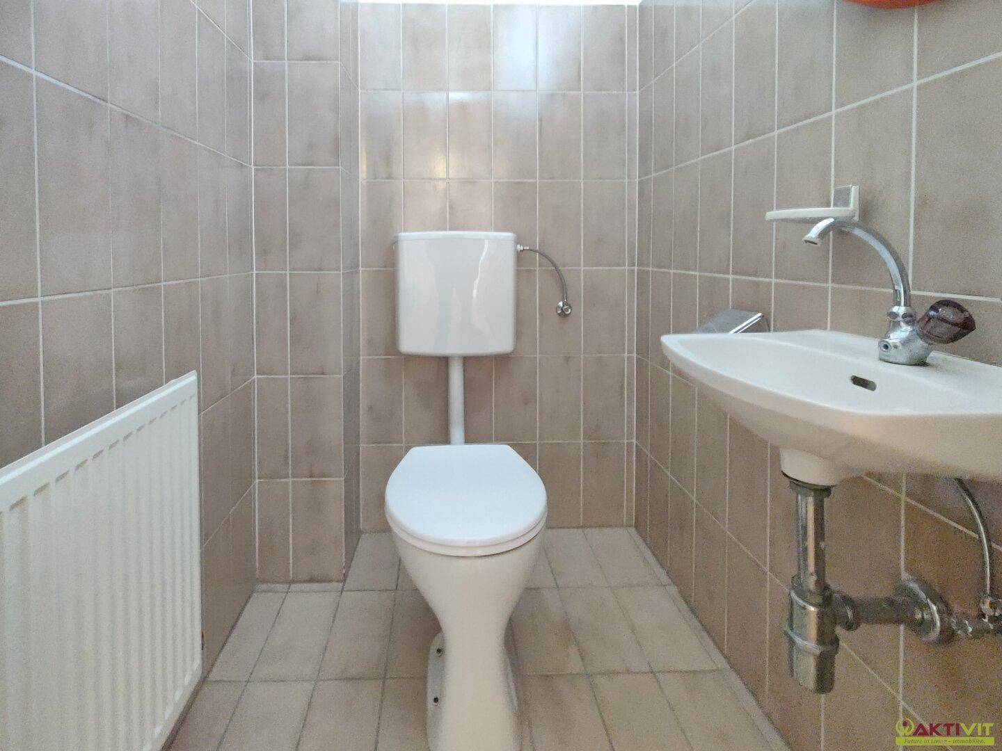 Kleines, gefliestes Gäste-WC mit Toilette und Waschbecken in neutralen Beigetönen.